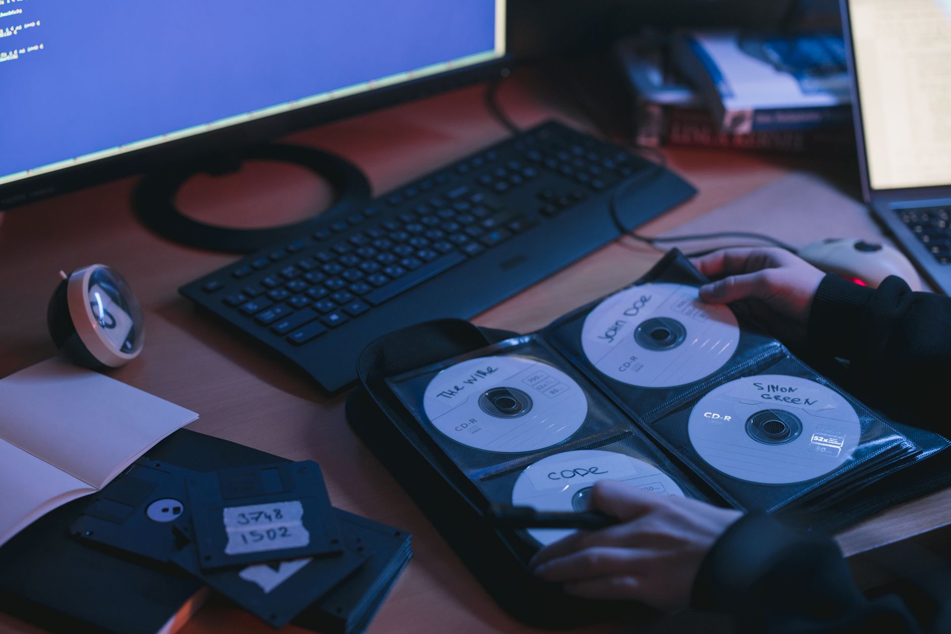 Płyty CD na biurku w biurze technologicznym, dłonie przy komputerze