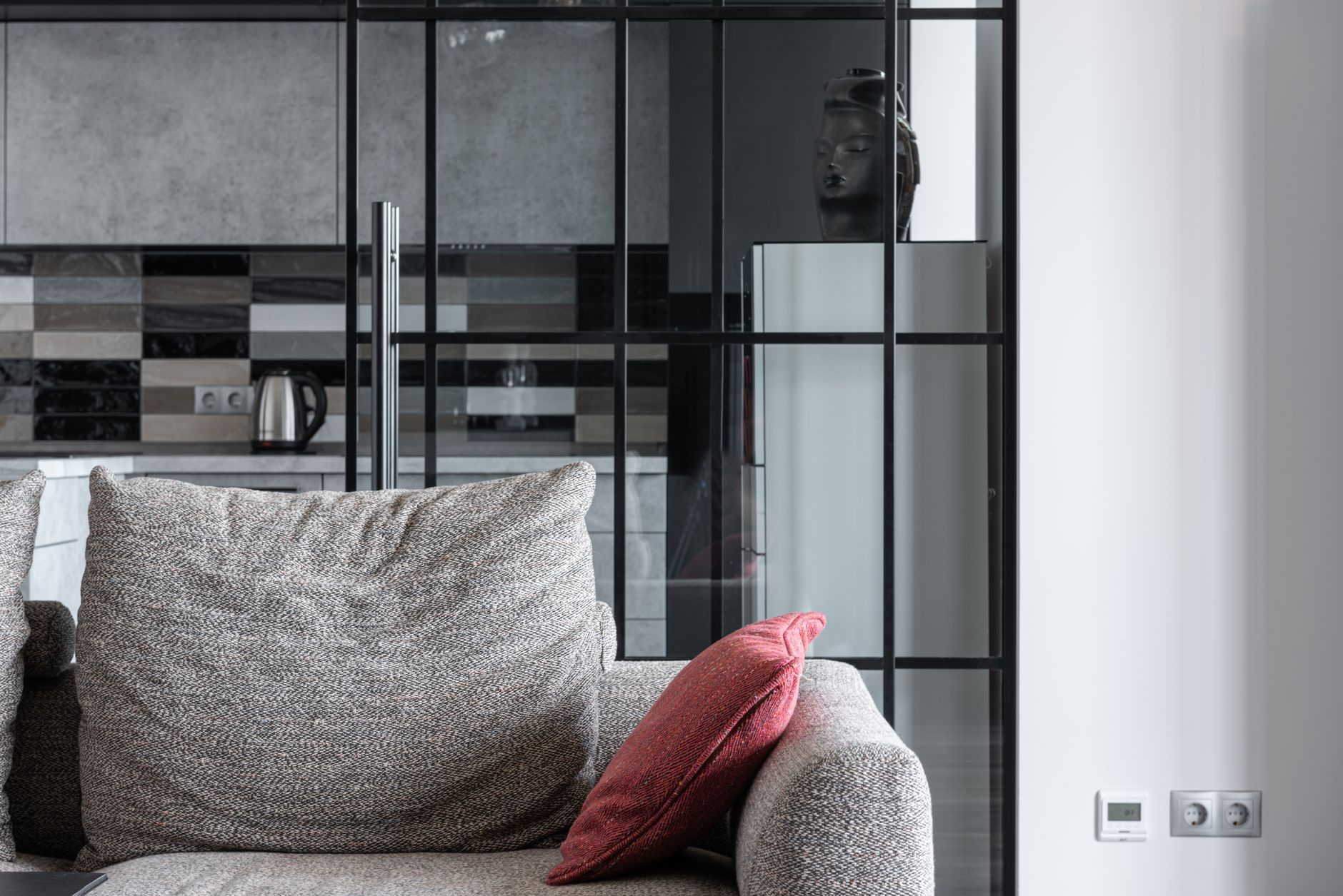 Przytulny salon z szarą sofą, czerwonym poduszką i nowoczesną kuchnią w tle