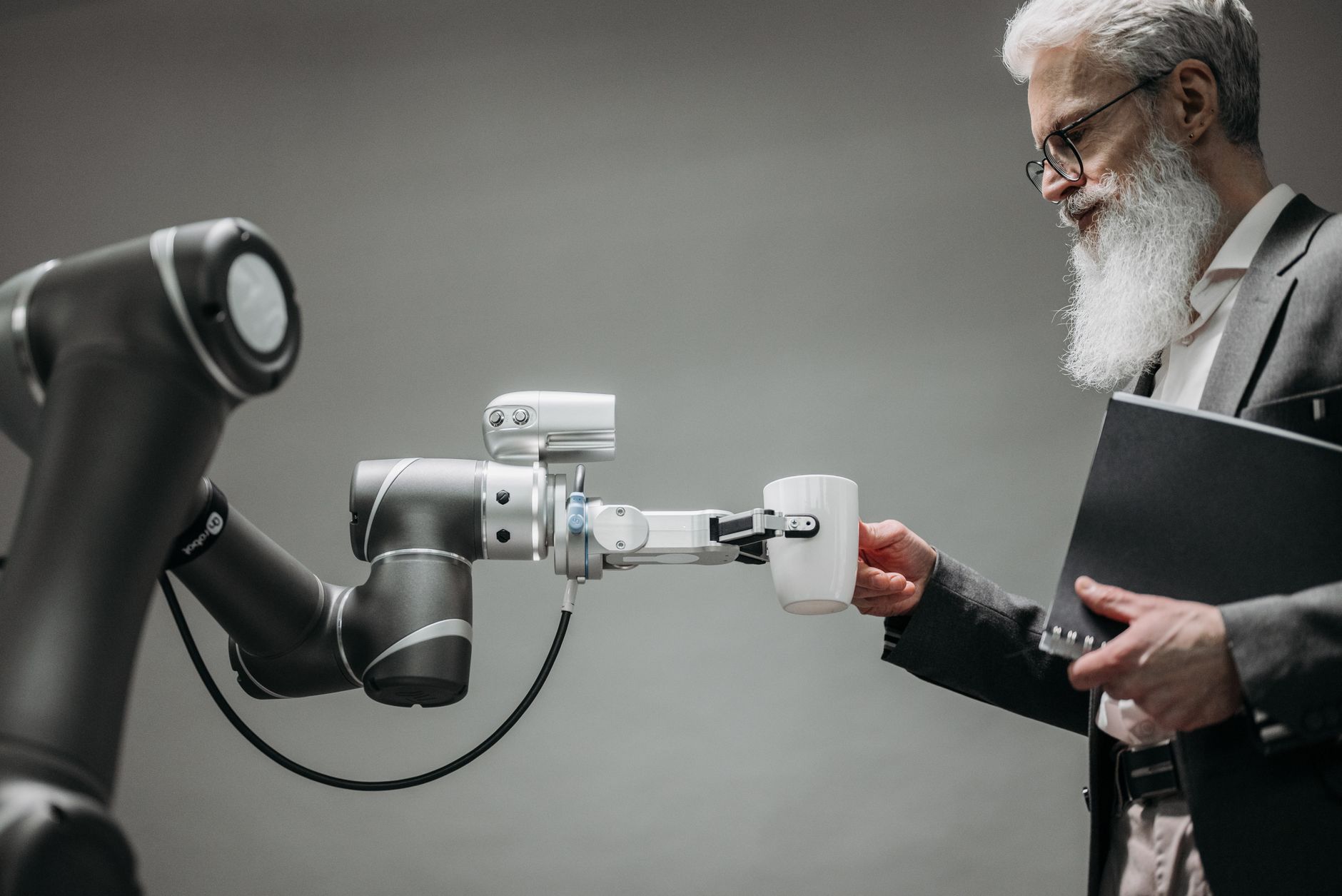 Starszy mężczyzna odbiera filiżankę od ramienia robota w biurze